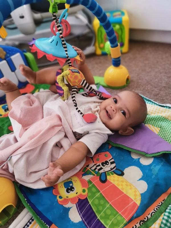 Baby lying on a colorful play mat, smiling and reaching for hanging toys. Baby lying on a colorful play mat, smiling and reaching for hanging toys.