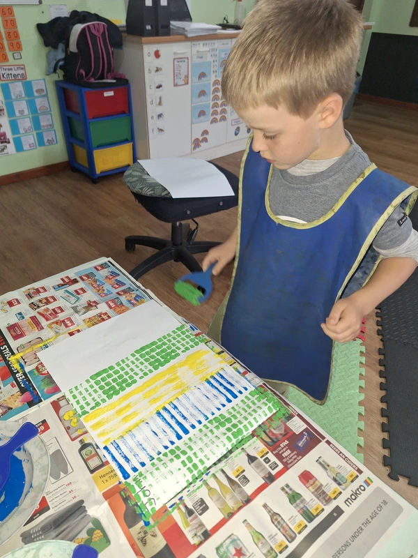 A young boy wearing a blue apron looks intently at a table, exploring what's on it. A young boy wearing a blue apron looks intently at a table, exploring what's on it.