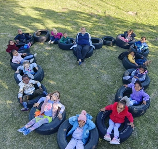 A group of kids sitting in a heart shape on a tire, smiling and enjoying their time together in a fun outdoor setting.