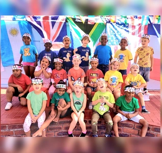 Children standing together, smiling for a photo with bright flags behind them, creating a cheerful atmosphere.