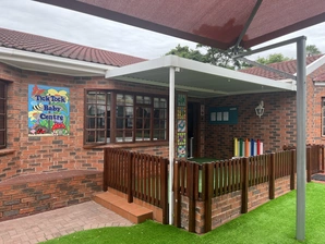 A quaint brick structure featuring a red roof, enclosed by a rustic wooden fence, amidst a serene landscape.