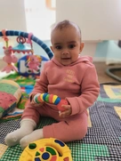 A cute baby sits on a colorful rug, happily playing with a bright toy in front of them.