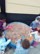 A cheerful group of children having fun in a sand pit, digging and playing with toys on a bright, sunny day.