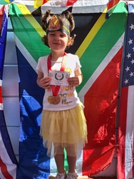 A cheerful little girl displays her medal while standing proudly in front of the South African flag, radiating joy and accomplishment.