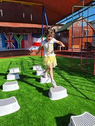 A cheerful young girl leaps on a stack of blocks, having a great time while playing and enjoying her surroundings.
