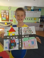 A young boy holds up a vibrant drawing of a street, smiling as he shares his artwork with others.