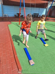 Two kids having fun on a playground, climbing and swinging while surrounded by bright equipment and green grass.