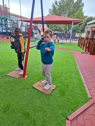 A young boy happily stands on a swing, enjoying the sunny day at the playground.